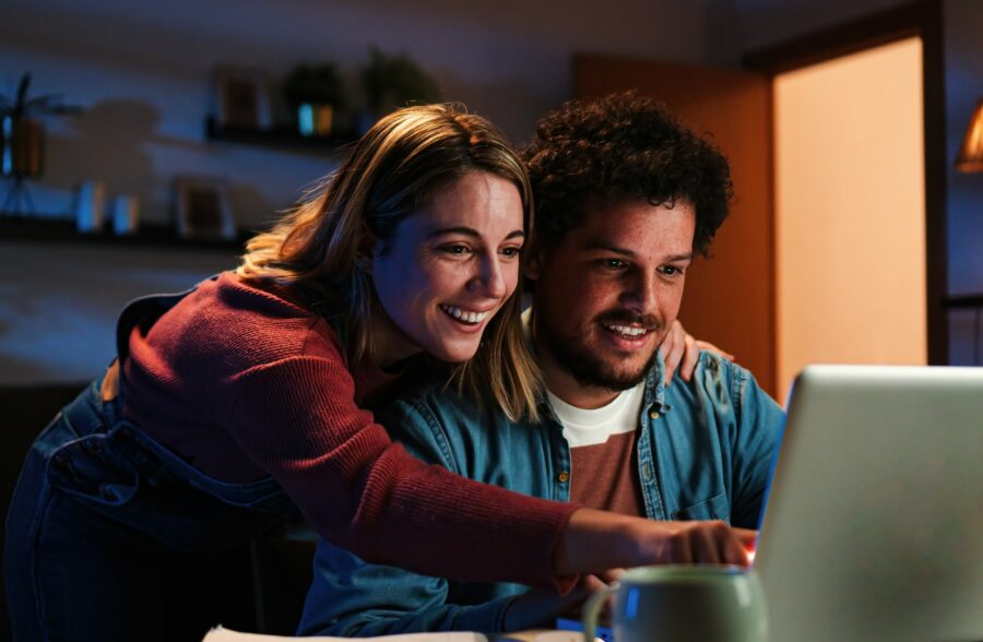 Young happy caucasian couple browsing on internet using a laptop to search sale at home. Excited