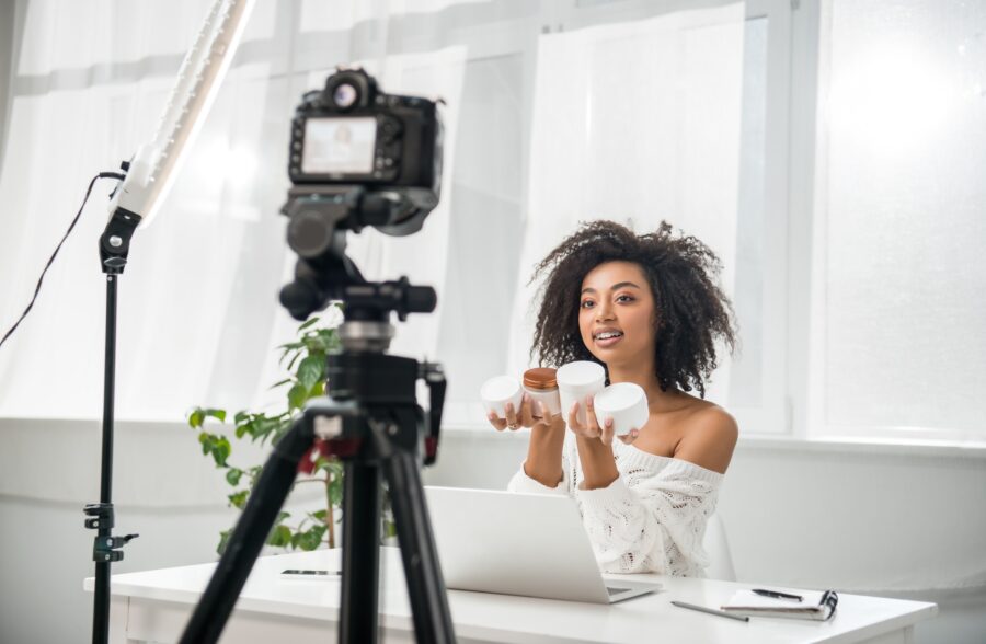 selective focus of attractive african american influencer in braces holding containers with cosmetic