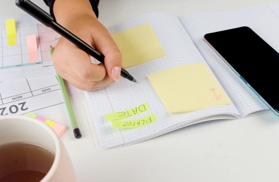 Girl Hands With Mobile Phone With Calendar Writing And List Of Work In Diary On Desk